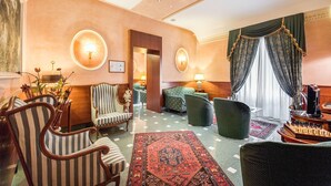 A hotel lobby with striped armchairs, a green sofa, a chess table, and a red patterned rug. - Hotel Giorgi (Rome)