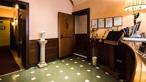 A hotel lobby with a reception desk, a marble statue, framed certificates on the wall, and a patterned floor. - Hotel Giorgi (Rome)