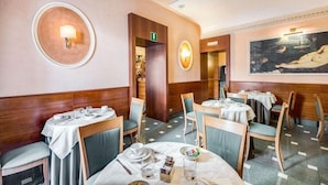 A restaurant with round tables, chairs, and a painting on the wall. - Hotel Giorgi (Rome)