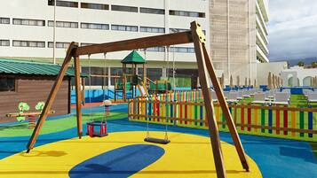 A playground with swings and slides, surrounded by a colorful fence, with a building in the background.