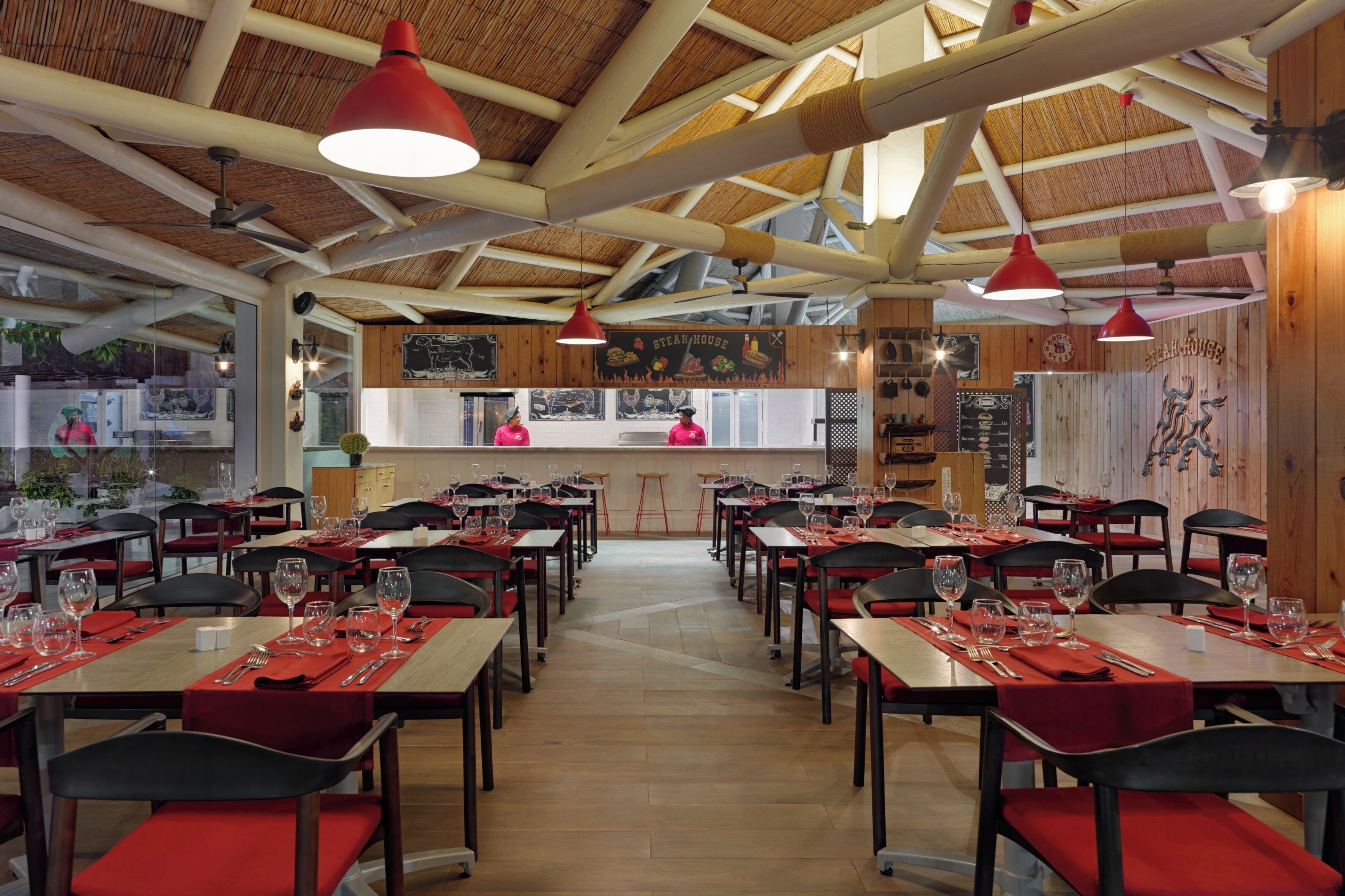 A restaurant with multiple tables and chairs, a bar area, and a high ceiling with exposed beams.