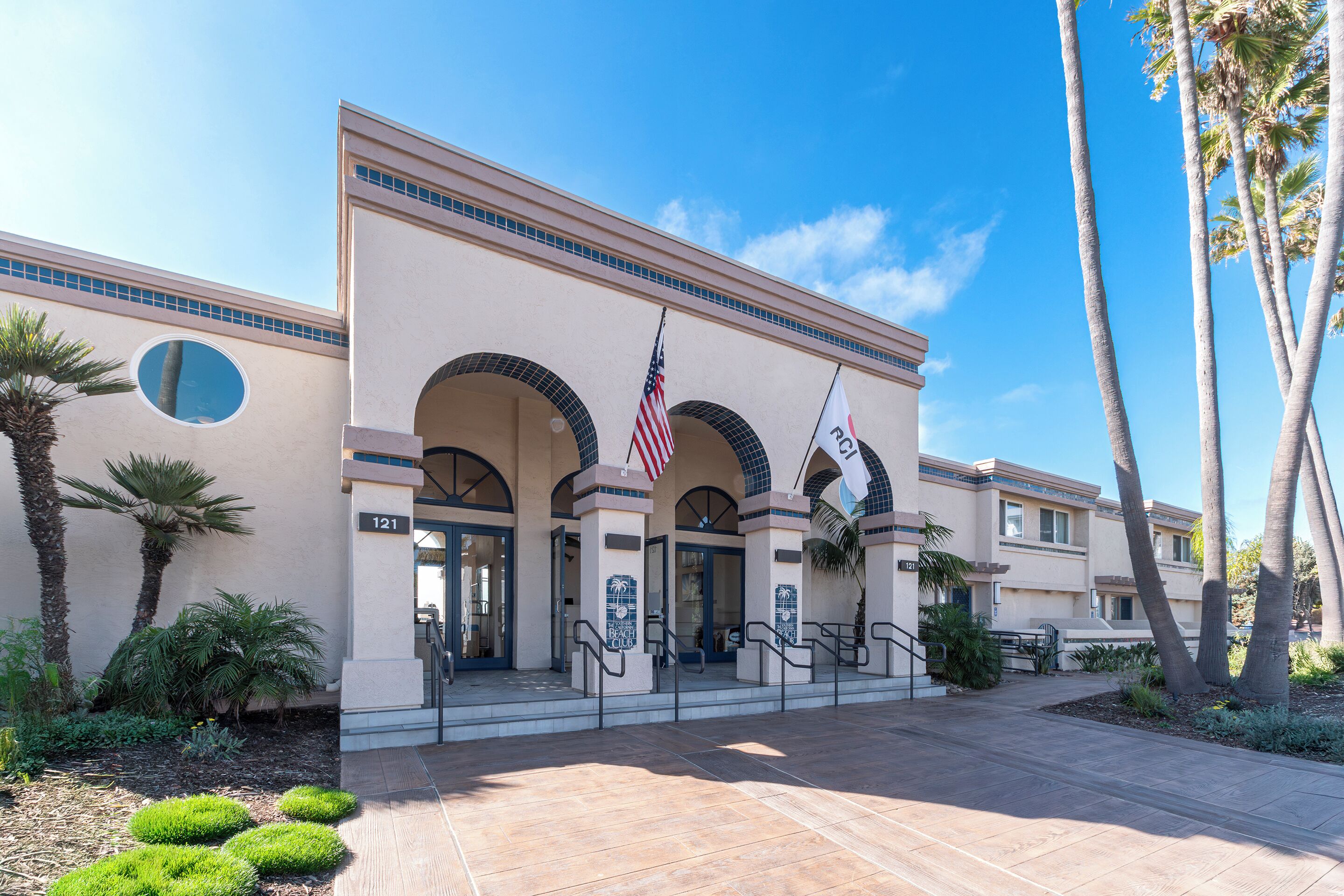 A hotel entrance with a large American flag, palm trees, and a clear blue sky.