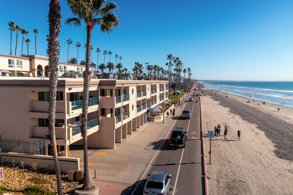 Un hotel frente a la playa con varios balcones, zona de estacionamiento y vistas a la playa.