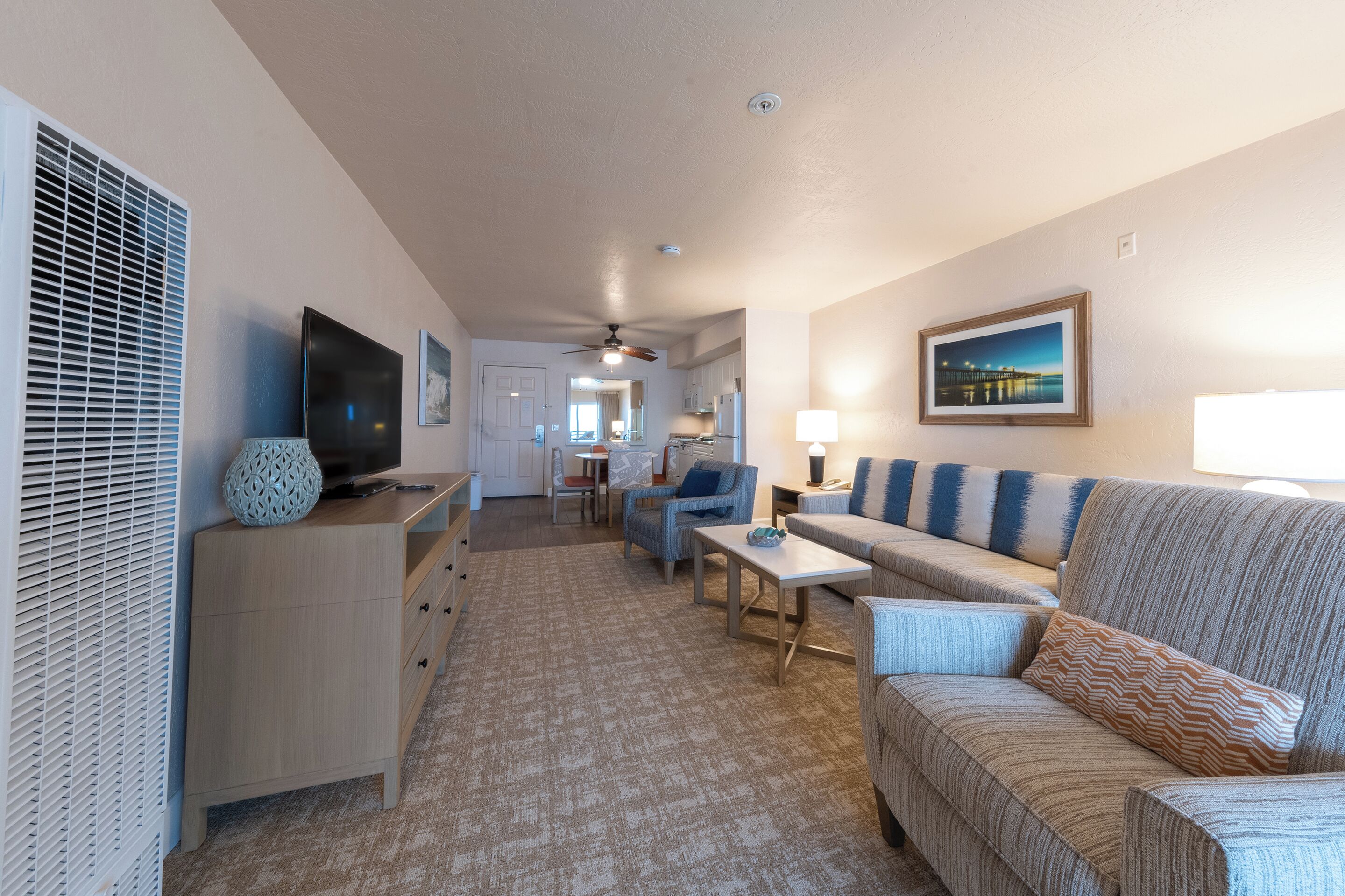A well-lit living room with a sofa, a television, and a dining area in the background.