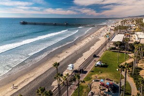 A beach with a pier extending into the ocean, a playground, and a road parallel to the beach. - Southern California Beach Club (Oceanside)