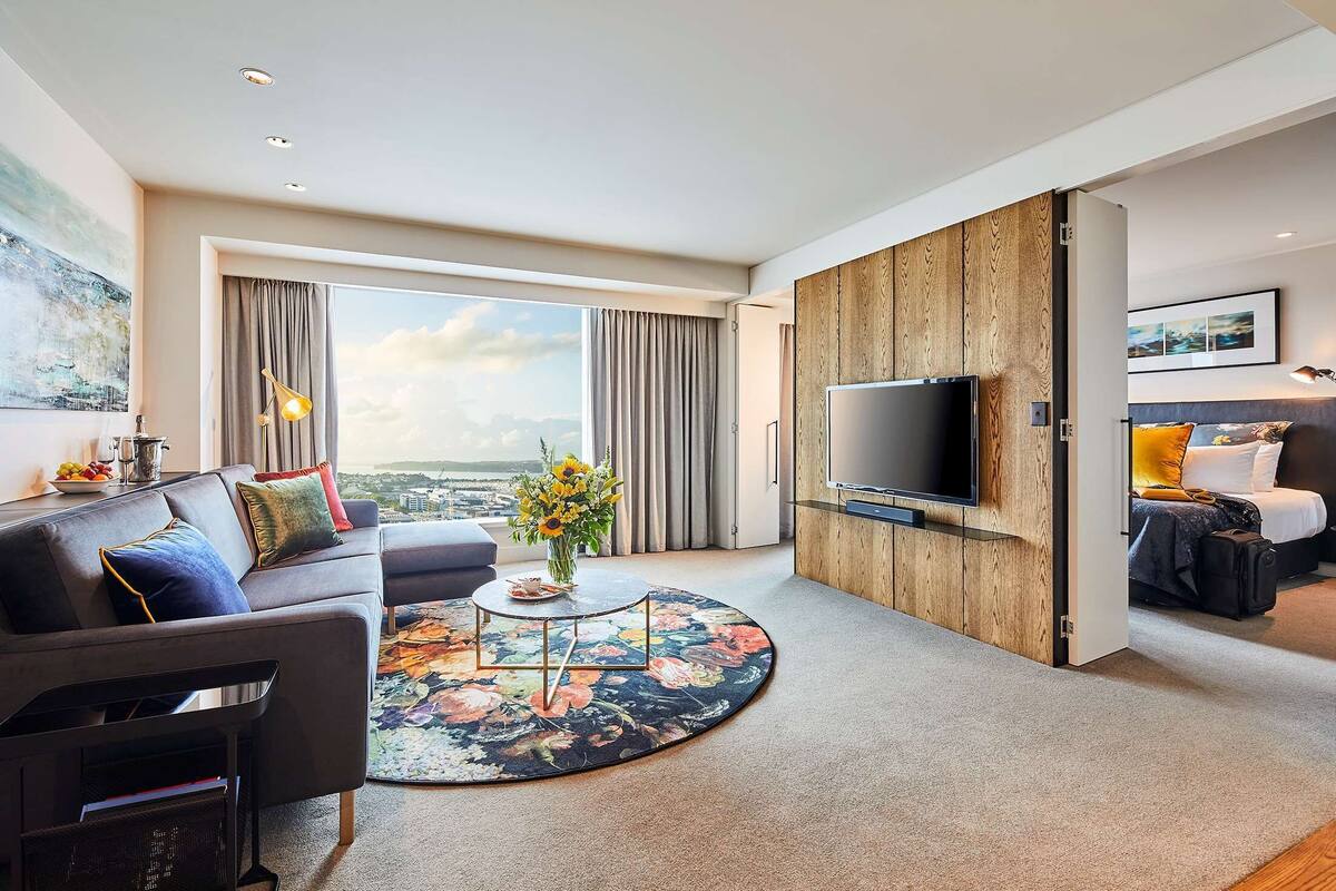 A modern living room with a large TV, a sofa, a coffee table, and a view of the city.