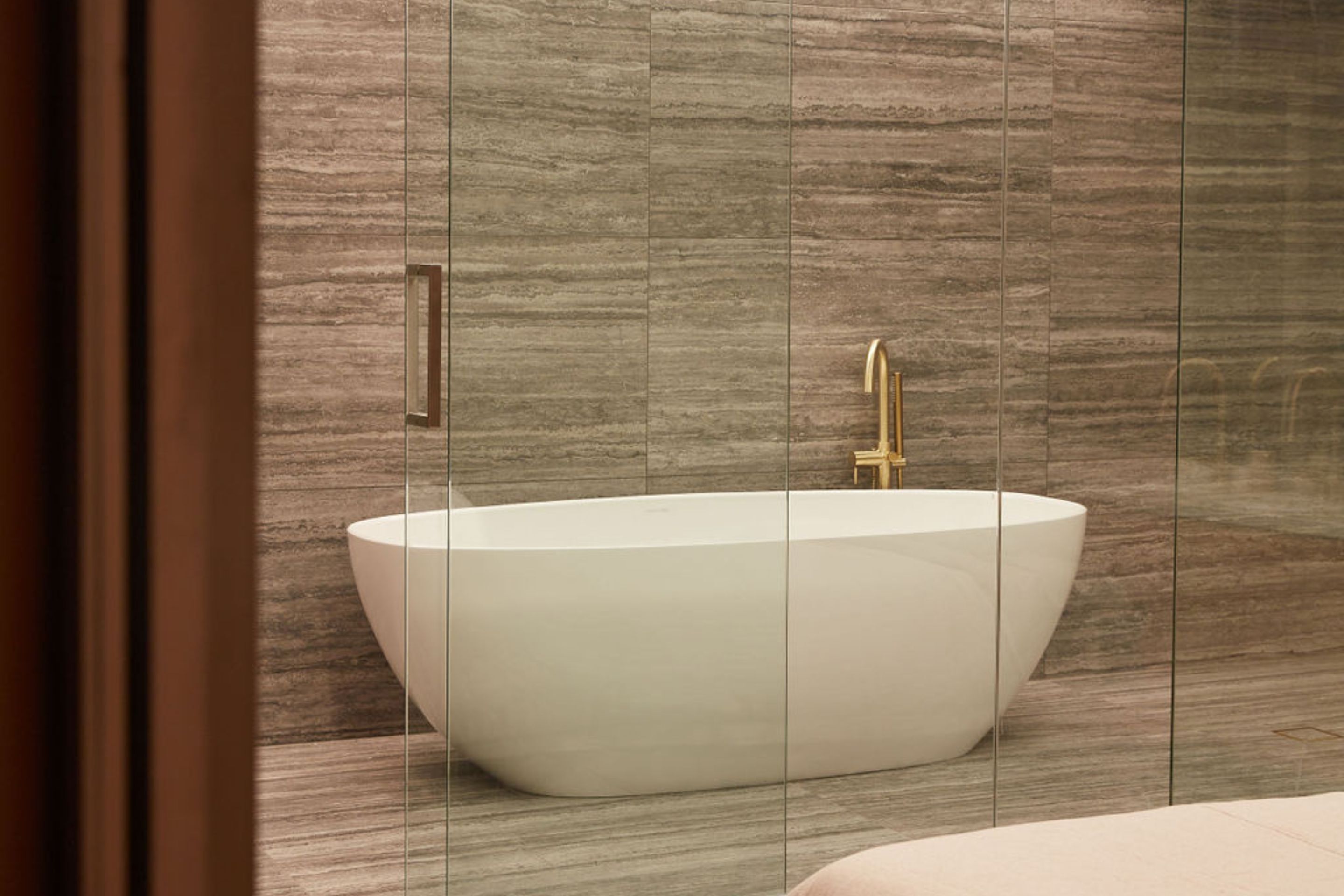 A modern bathroom with a freestanding bathtub, a gold faucet, and a wooden floor.