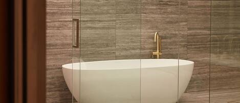 A modern bathroom with a freestanding bathtub, a gold faucet, and a wooden floor.