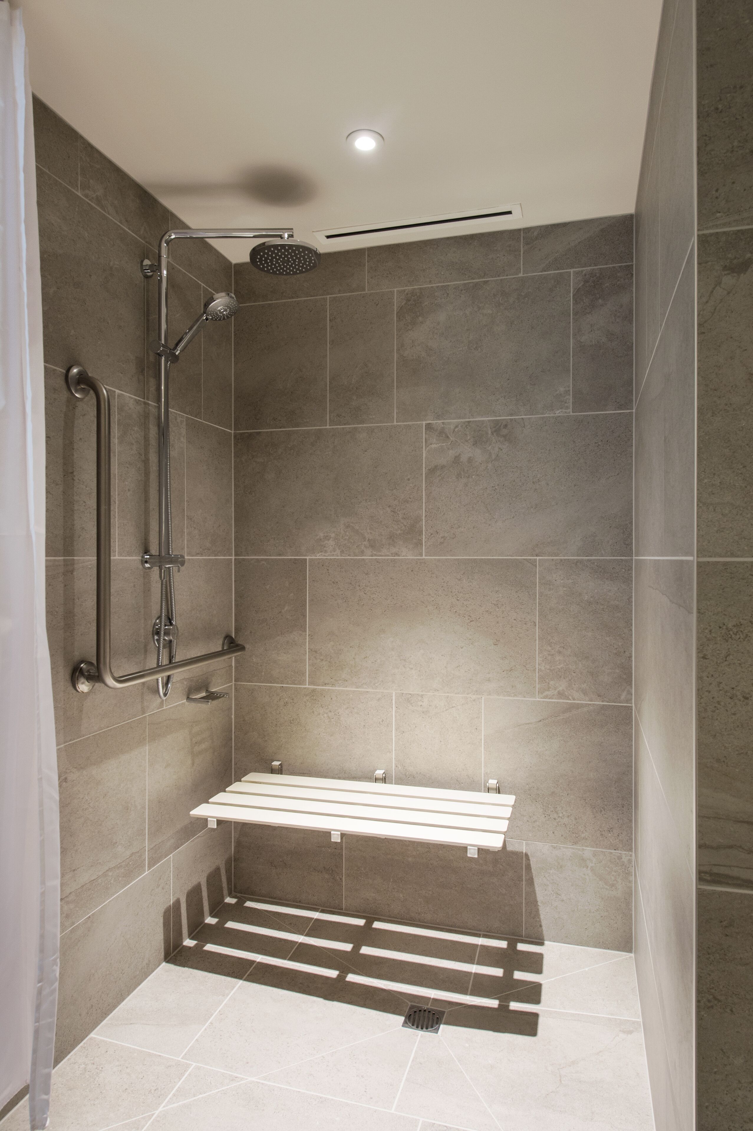 A shower area with a bench, grab bars, and a handheld showerhead.