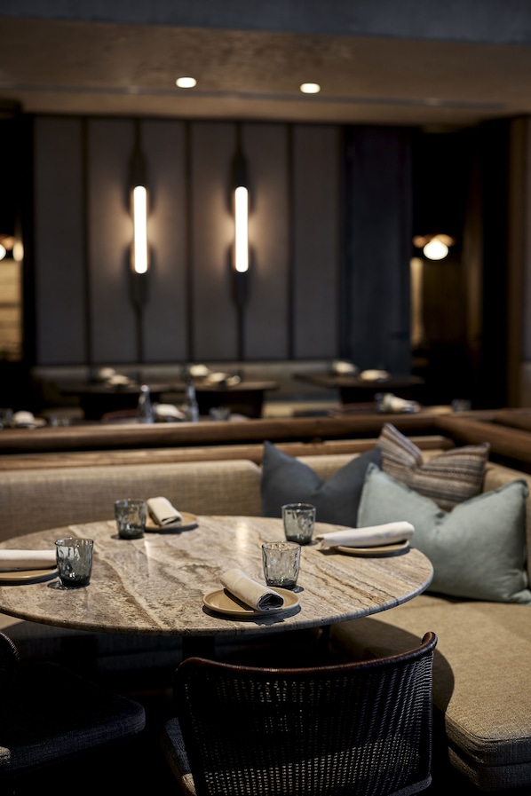 Ein Restaurantinneres mit runden Tischen, gepolsterten Sitzgelegenheiten und Pendelleuchten.