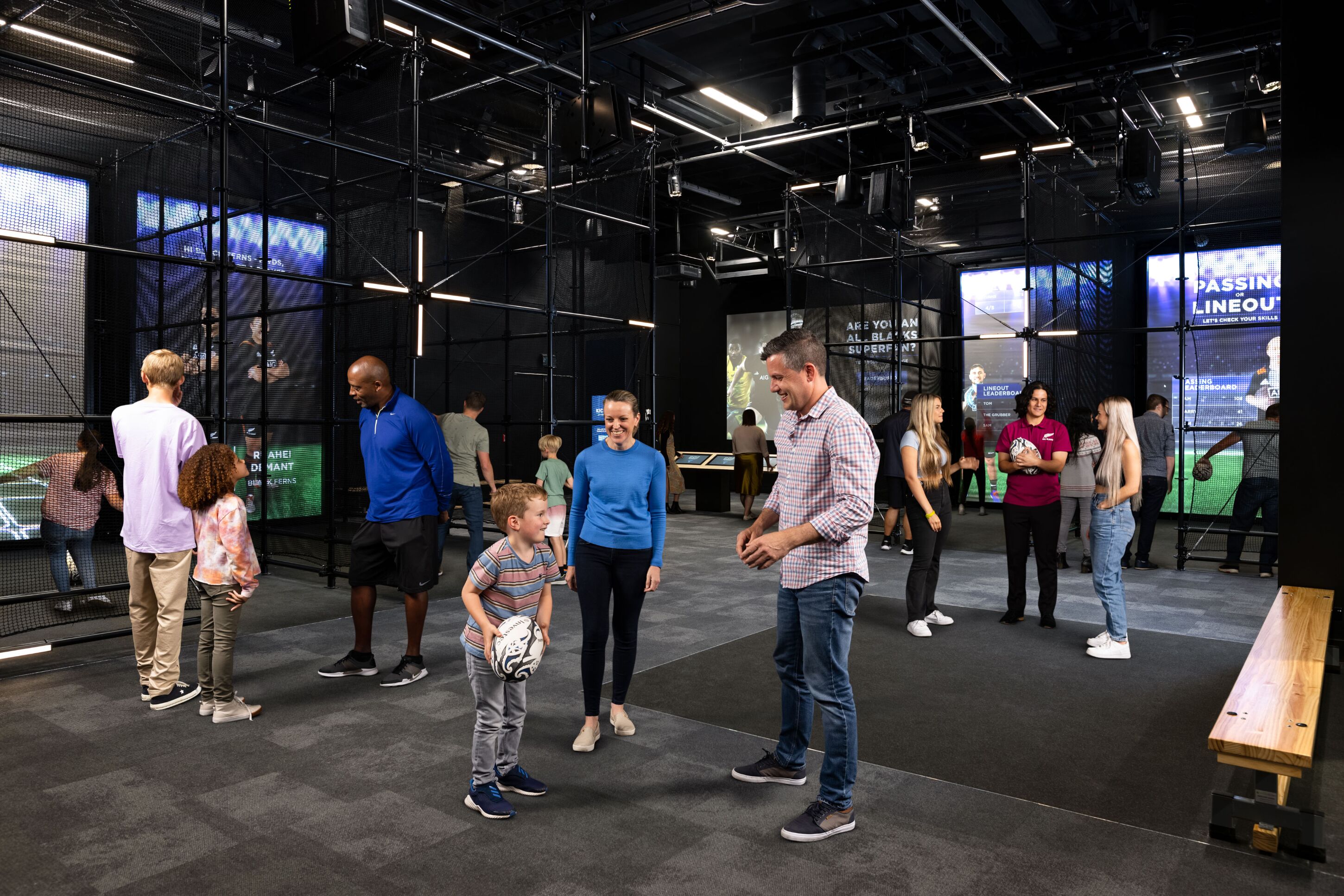 A modern indoor space with a high ceiling, visible structural beams, and large digital screens displaying content.