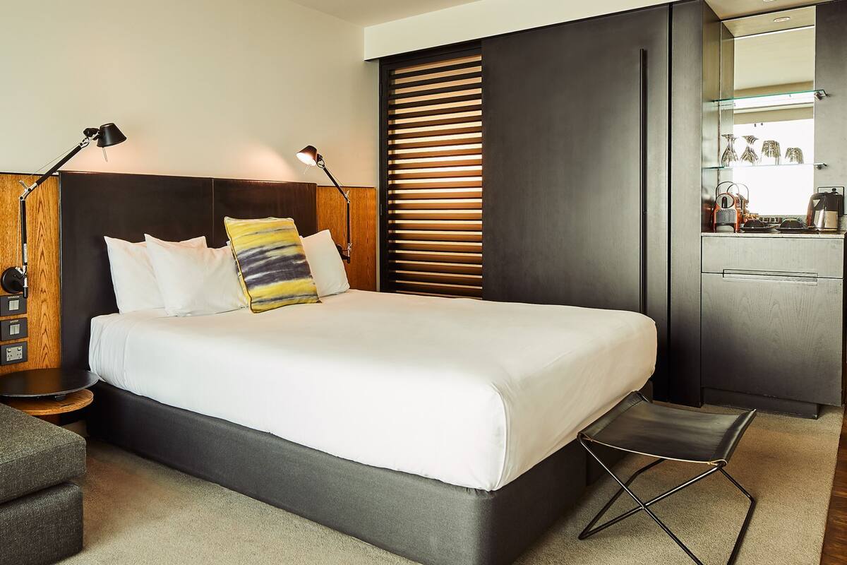 A modern hotel room with a large bed, a sofa, a desk, and a mirror.
