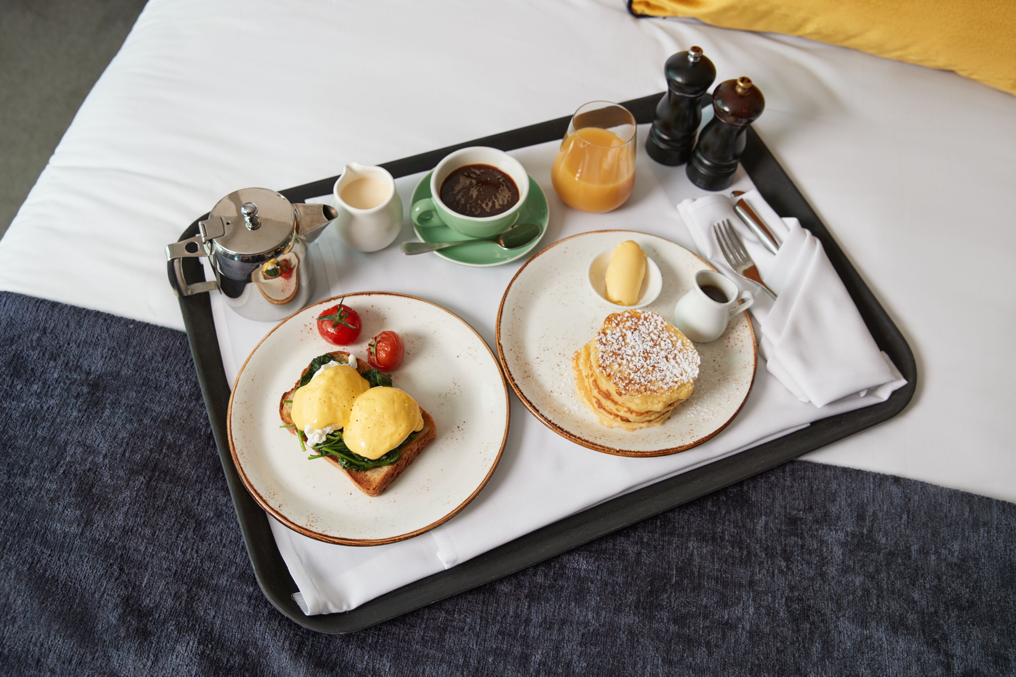 A breakfast tray with toast, eggs, a drink, and condiments on a bed.