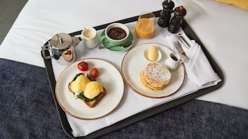 A breakfast tray with toast, eggs, a drink, and condiments on a bed.