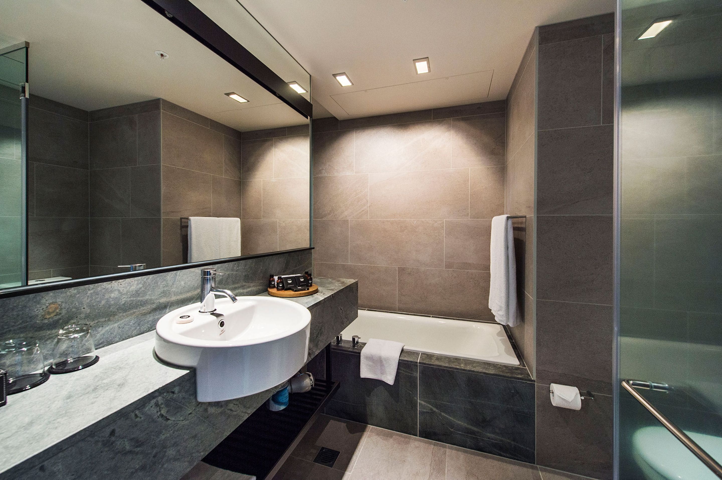 A modern bathroom with a large mirror, a sink, and a bathtub.