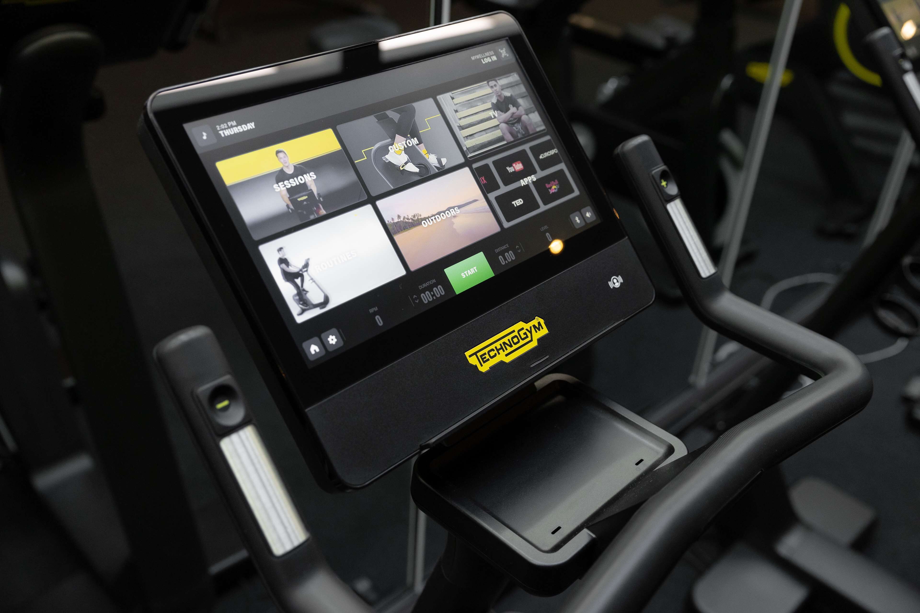 A treadmill with a digital display showing workout options and a "TECHNOGYM" logo.