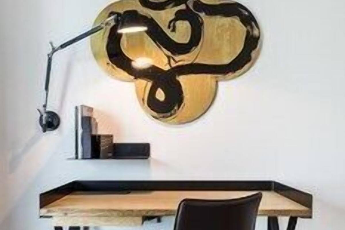 A desk with a chair, a lamp, and a wall-mounted abstract art piece.