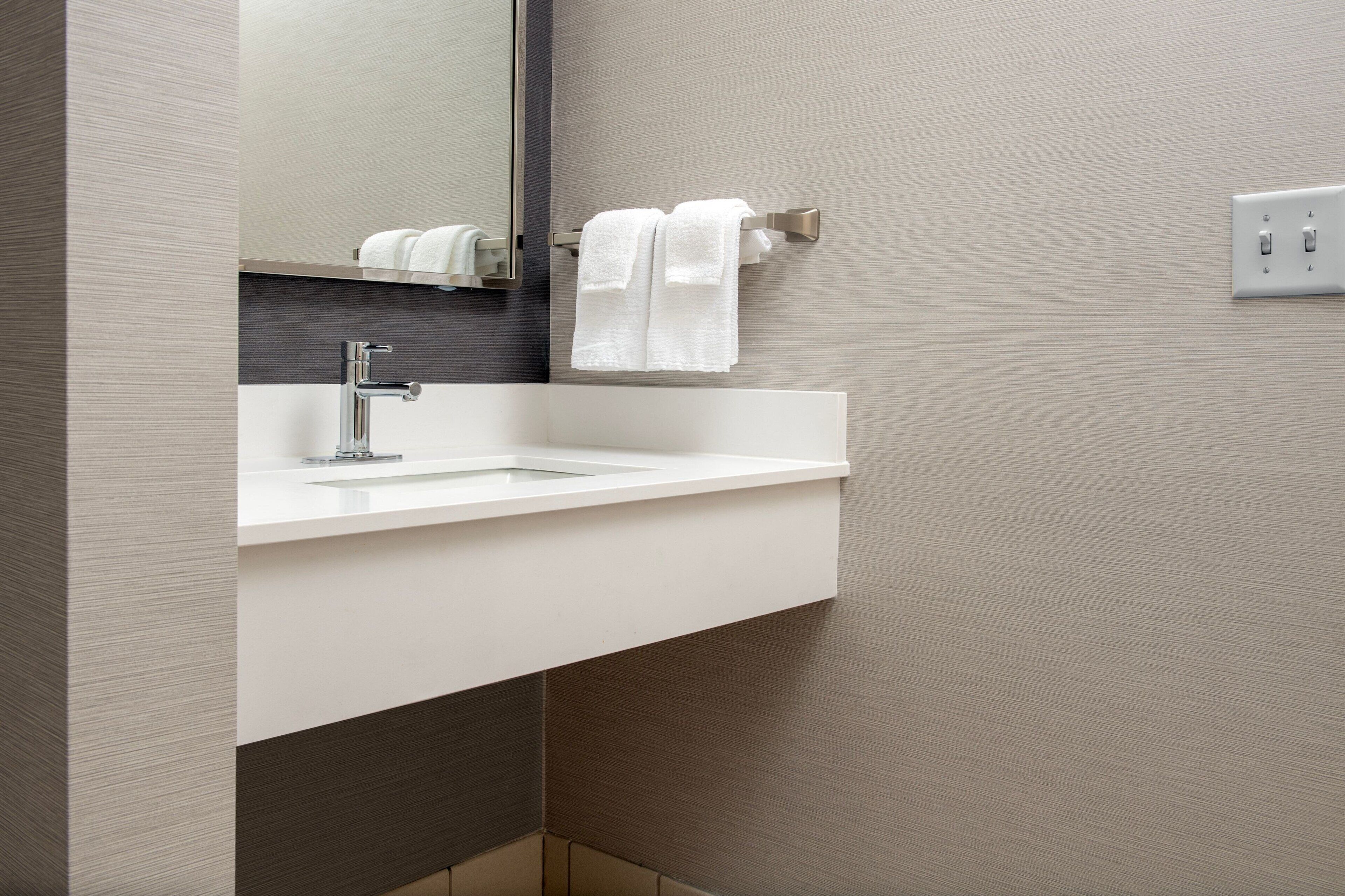 A modern bathroom with a white sink, a mirror, and two white towels hanging on a towel rack.
