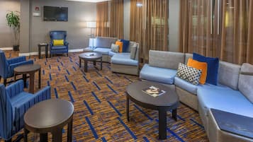 A hotel lobby with seating areas, a flat-screen TV, and a patterned carpet.