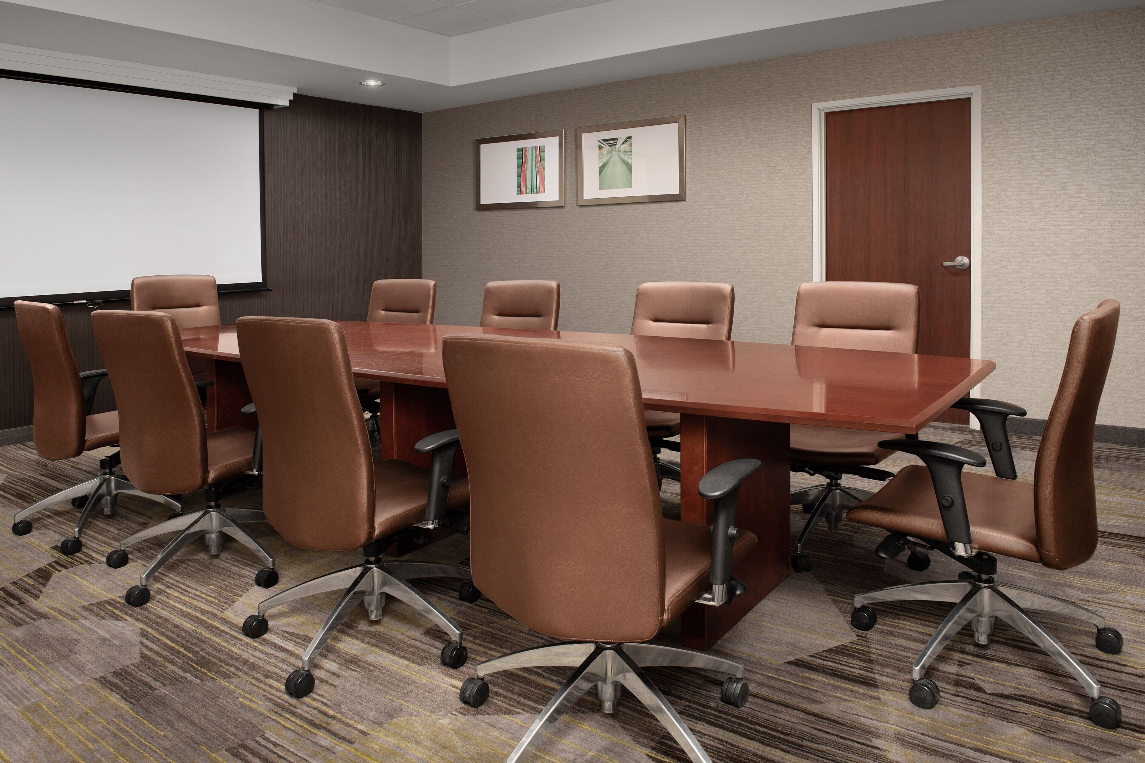 A conference room with a large table and eight brown chairs with wheels.