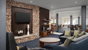 A modern lounge area with a stone accent wall, a flat-screen TV, a blue sofa, and a glass coffee table. - Courtyard by Marriott Panama City (Panama City)