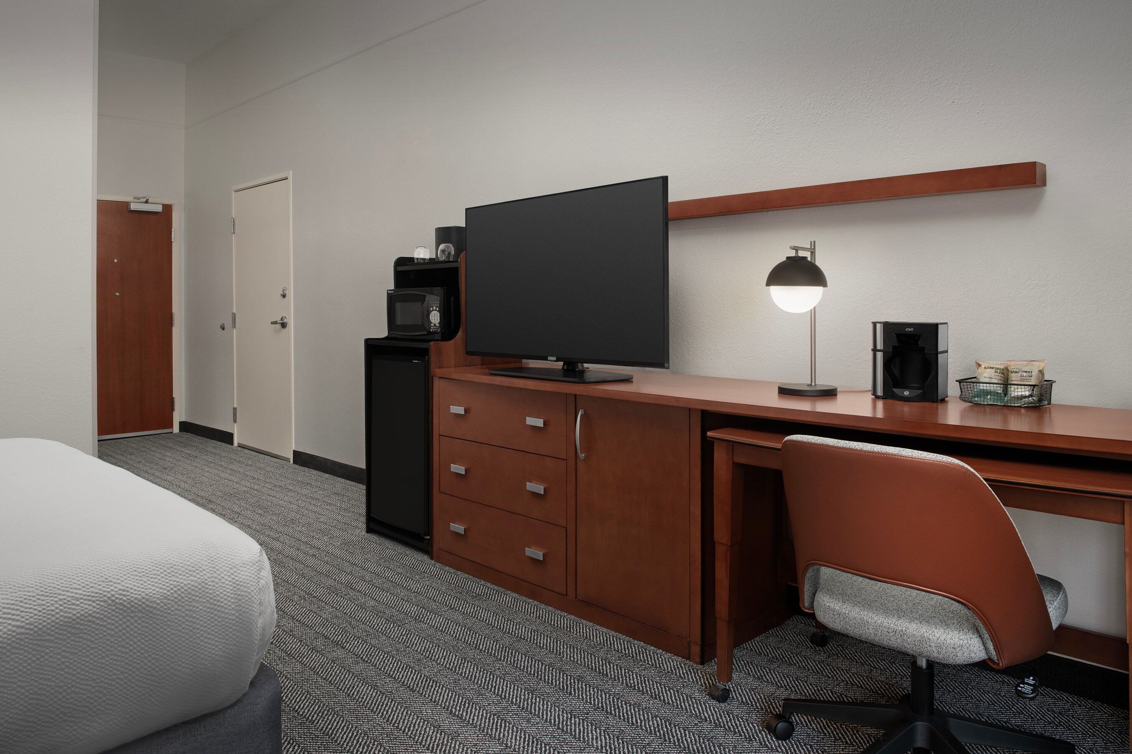 A hotel room with a bed, a desk with a television, a coffee maker, and a lamp.