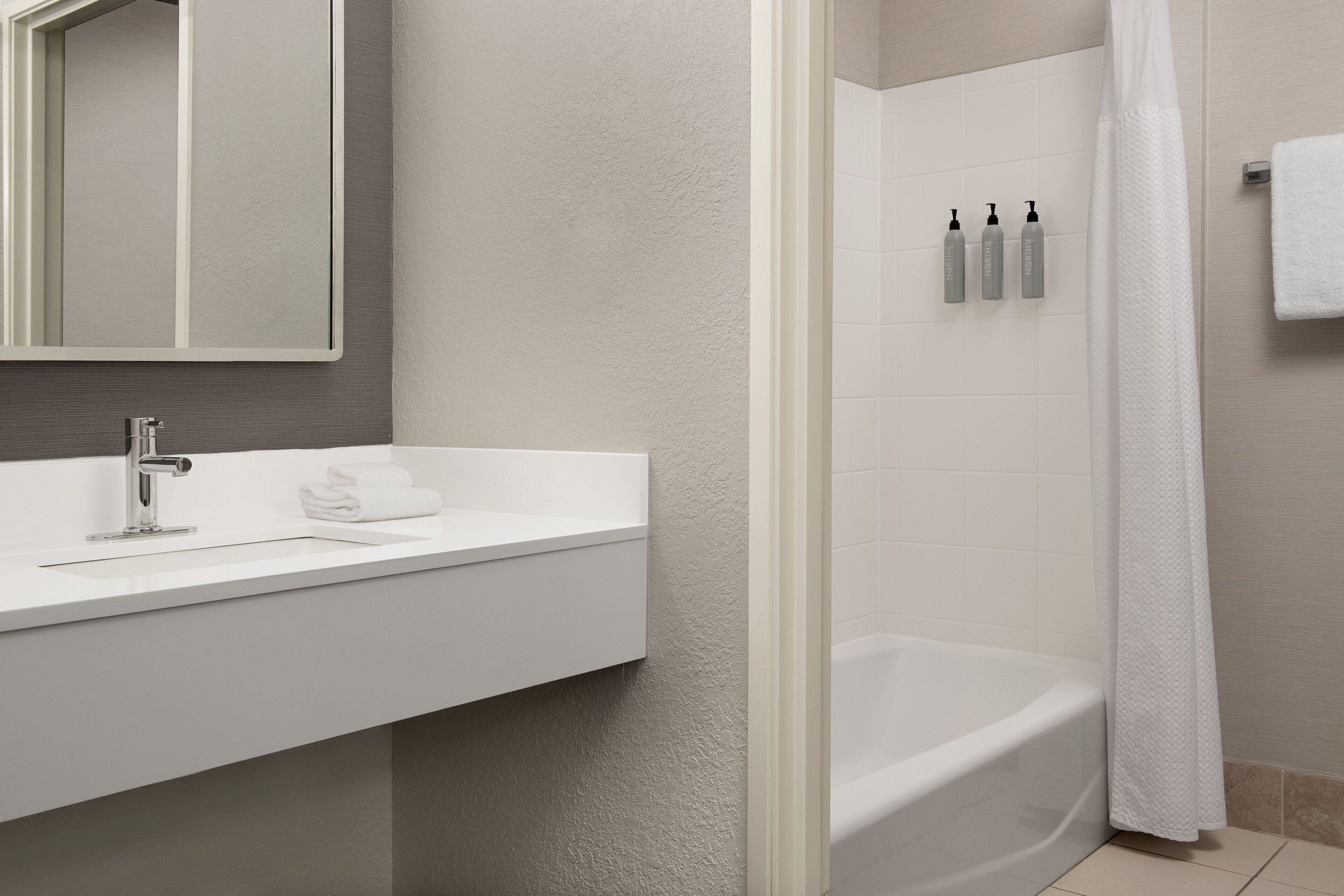 A modern bathroom with a white sink, a mirror, a shower curtain, and toiletries on the wall.