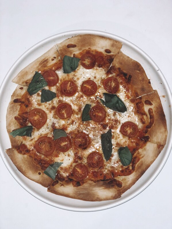 A pizza with tomato slices and basil leaves on a white plate. - Pelican Waters Resort (Pelican Waters)