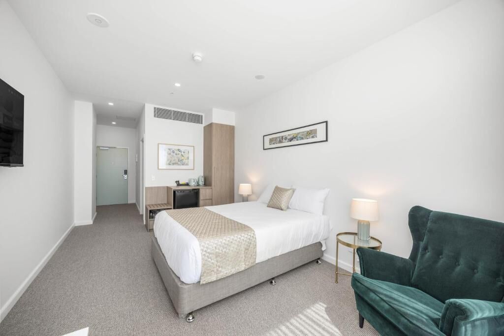 Quarto de hotel com uma cama, mesas de cabeceira, escrivaninha, cadeira e televisão.