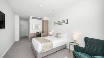 Quarto de hotel com uma cama, mesas de cabeceira, escrivaninha, cadeira e televisão.