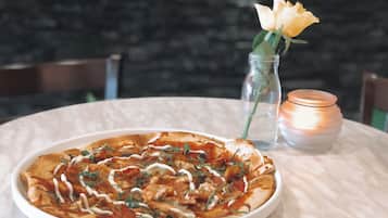 A pizza on a white plate with a glass of water and a candle on a table.