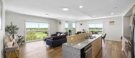 A modern kitchen with a central island, wooden flooring, and large windows offering a view of the outdoors.