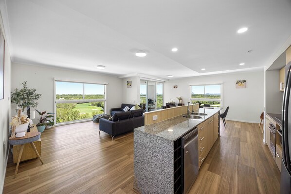 A modern kitchen with a central island, wooden flooring, and large windows offering a view of the outdoors. - Pelican Waters Resort (Pelican Waters)