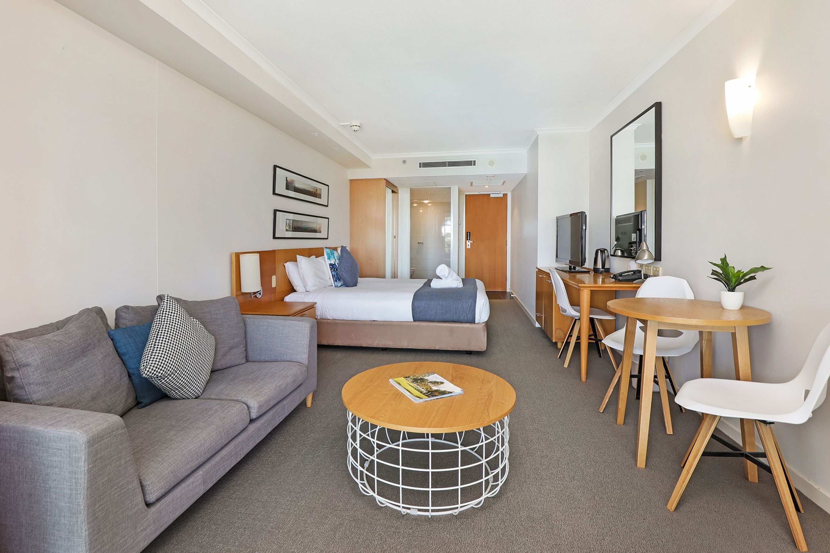 A hotel room with a bed, a sofa, a dining table, and a TV.