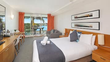 A hotel room with a bed, desk, and chair, a sofa, and a view of a pool.