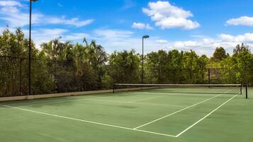 Un court de tennis avec un filet, entouré d’arbres et sous un ciel dégagé.