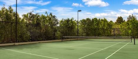 Cancha de tenis con red, rodeada de árboles y un cielo despejado.