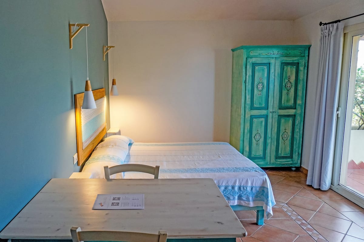 A room with a bed, a table with a chair, a wardrobe, and a window with curtains.