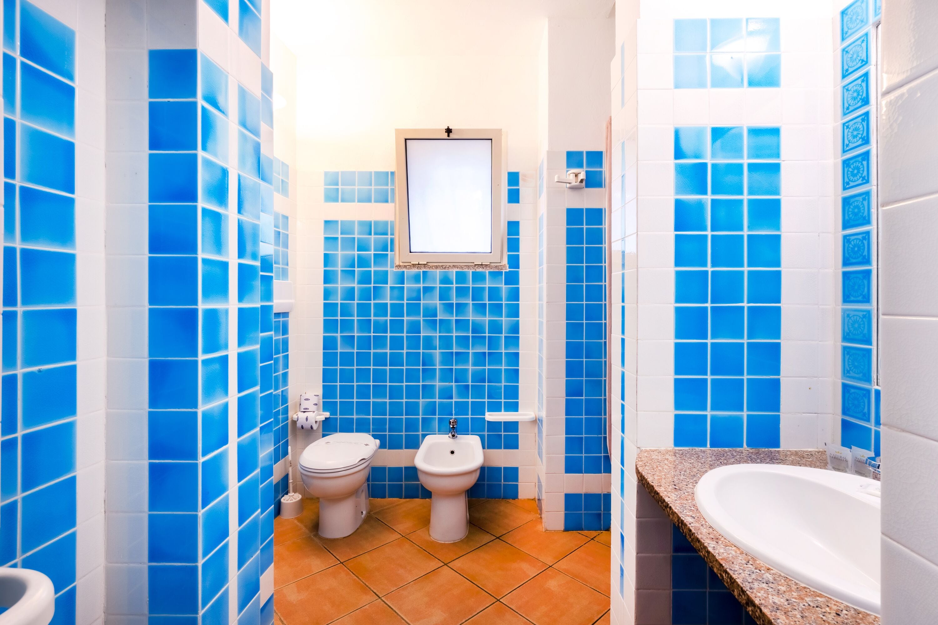 A bathroom with blue tiles, a white sink, and a white toilet.