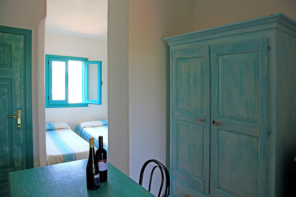 A room with a bed, a table with two bottles of wine, and a large blue cabinet.