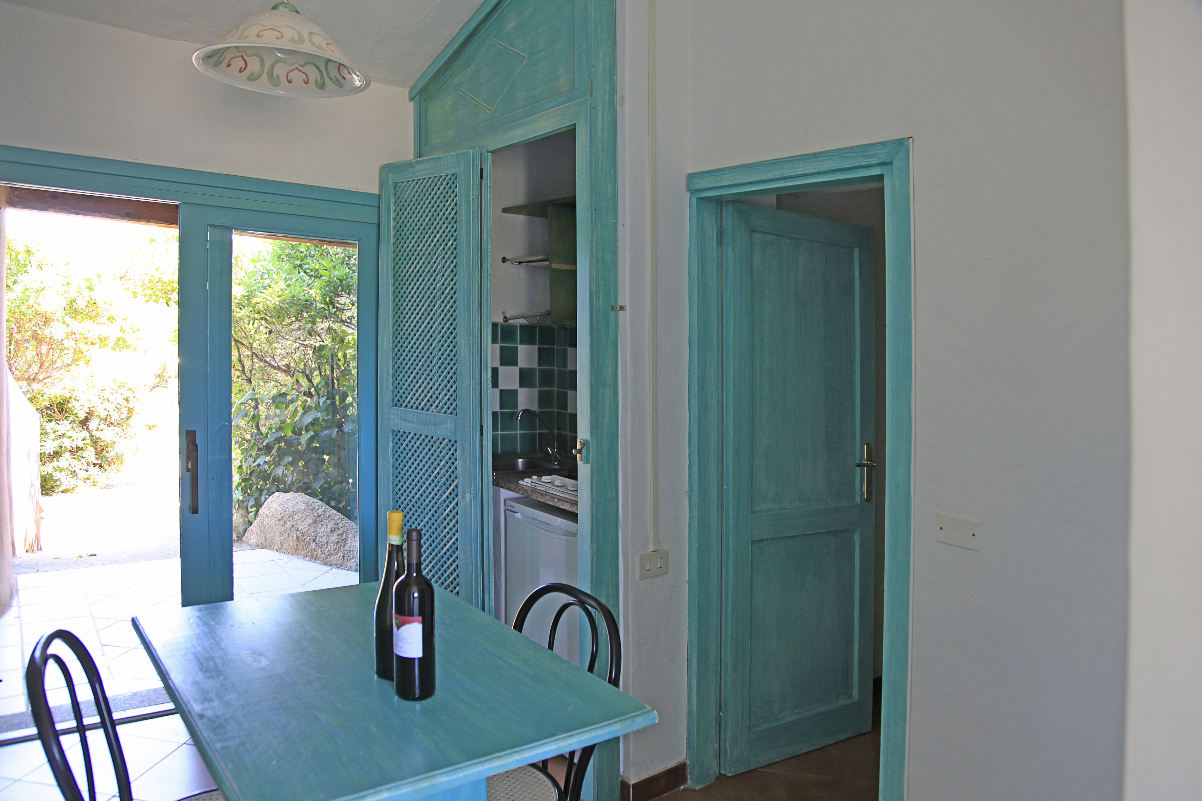 Un coin repas avec une table, des chaises et une bouteille de vin. On peut apercevoir une cuisine à travers une porte ouverte.