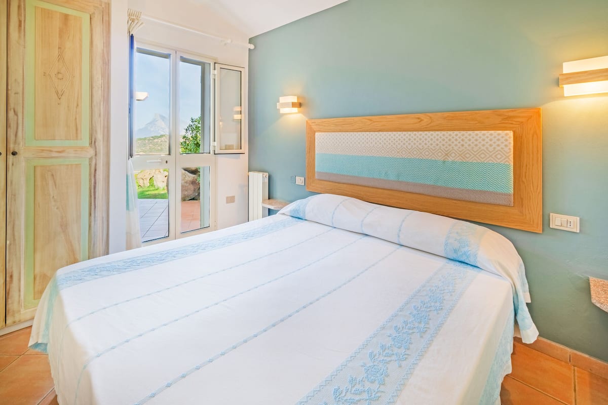 A bedroom with a large bed, a wooden headboard, and a view of a mountain through a glass door.