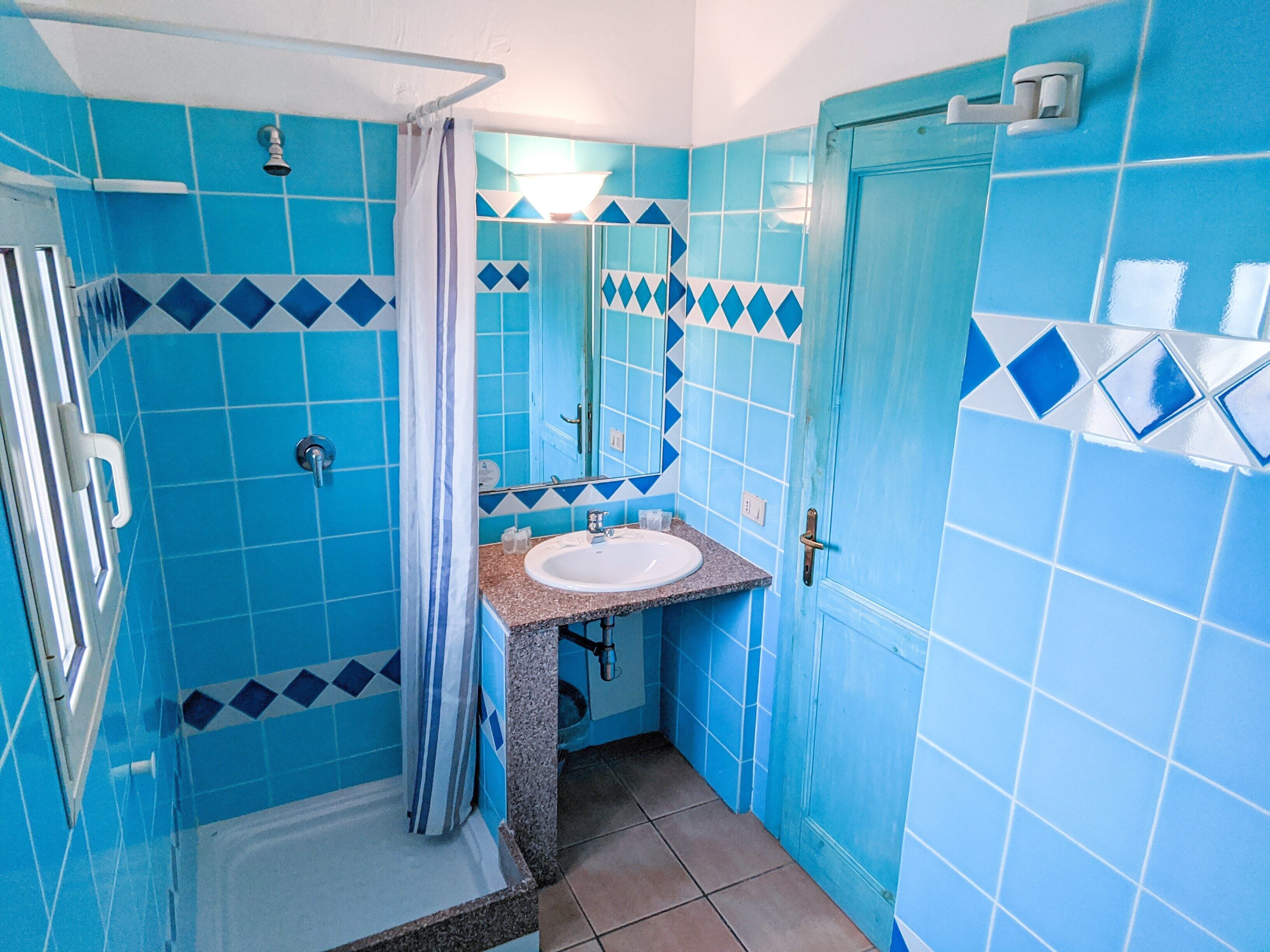 A bathroom with blue tiles, a shower, a sink, and a mirror.