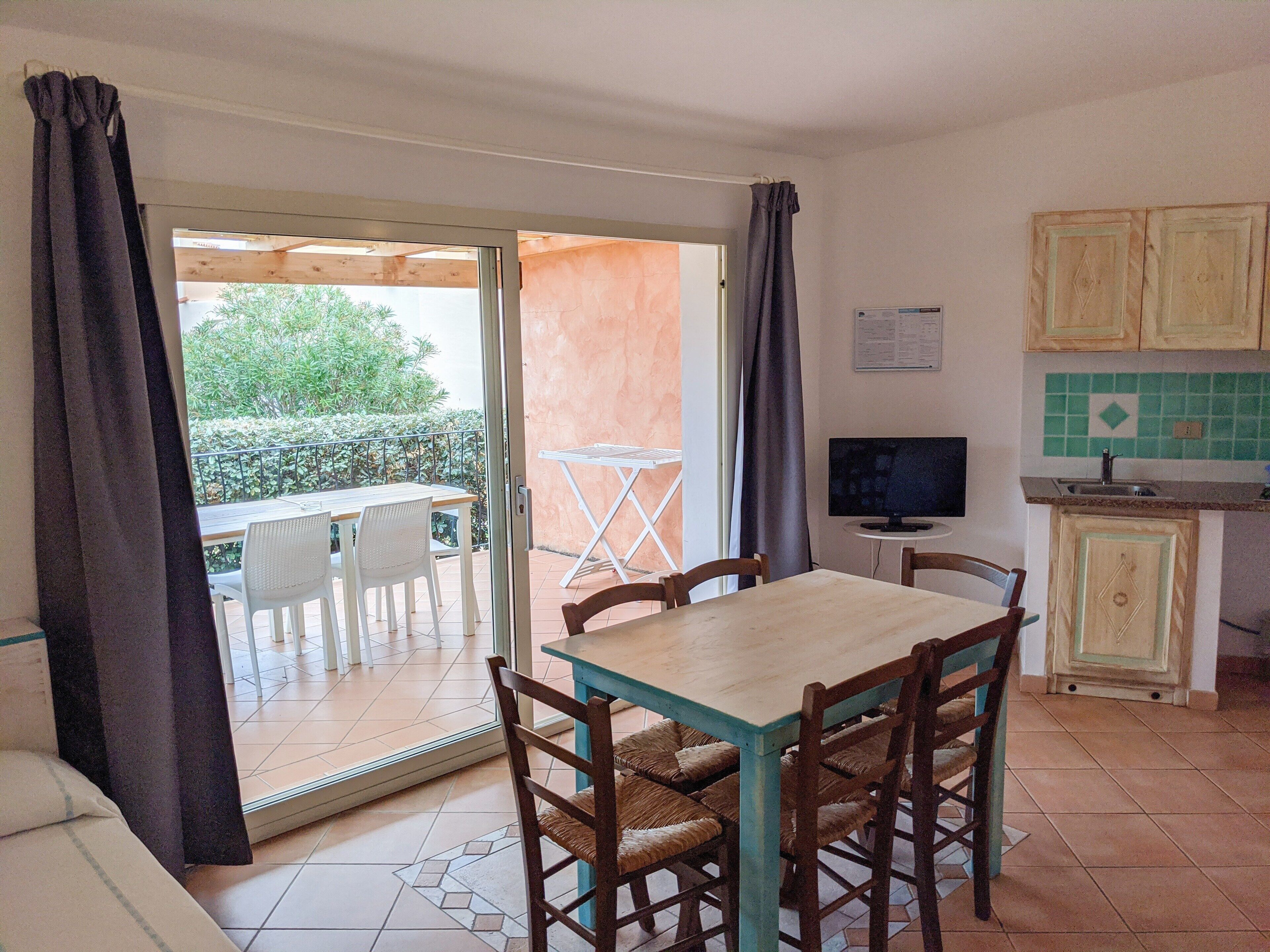 Un comedor con una mesa y sillas, un televisor y una cocina con armarios y salpicadero de azulejos.