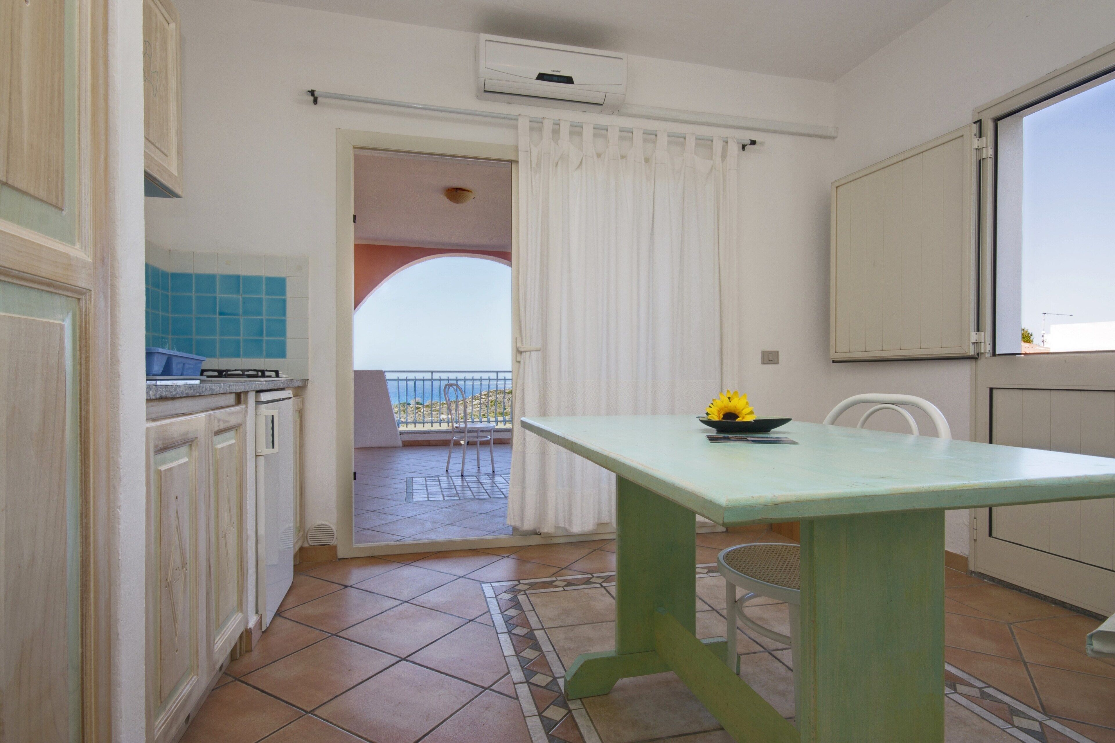 A kitchen with a dining table, a view to the outside, and a balcony with a chair.
