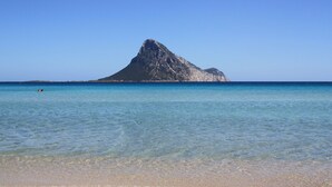 Vista despejada de una playa con una colina rocosa destacada al fondo.