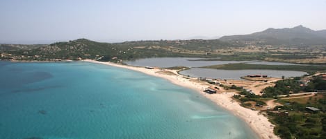Eine Luftaufnahme einer Küstenregion mit klarem, türkisblauem Wasser, einem Sandstrand und umgebender Vegetation.