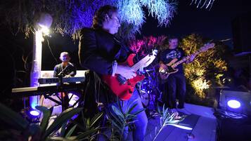 Una banda tocando al aire libre de noche, con iluminación de escenario e instrumentos musicales.