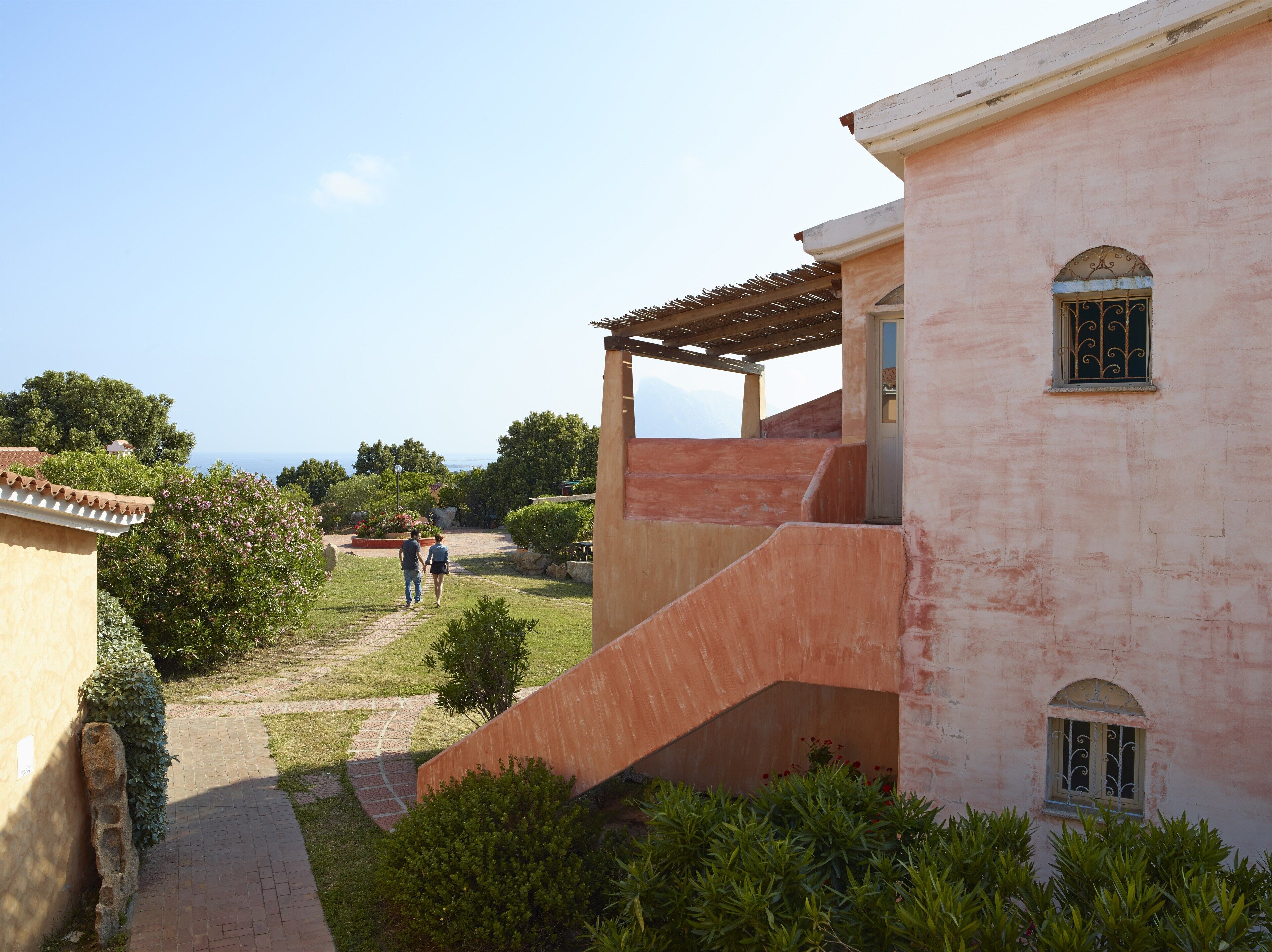 Un camí que condueix a un edifici amb una zona exterior coberta i vista al mar.