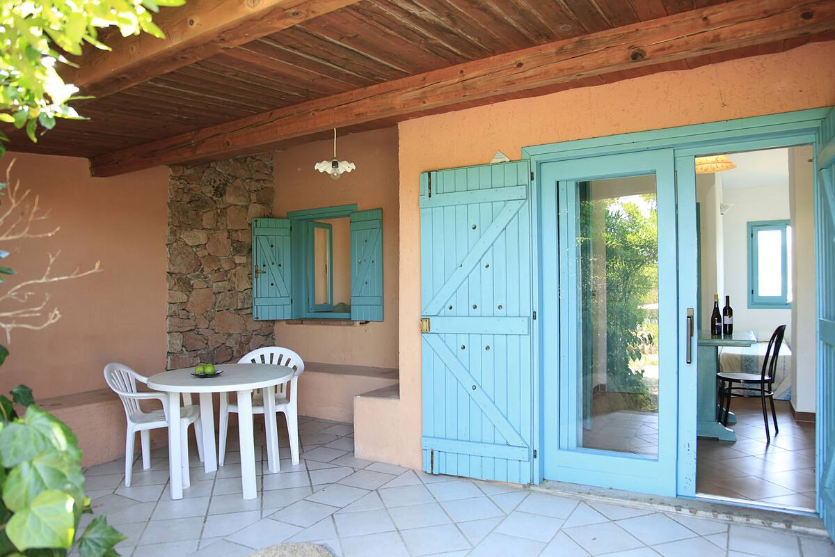 A patio with a stone wall, a table with chairs, and a blue door leading to an interior room with a table and chairs.